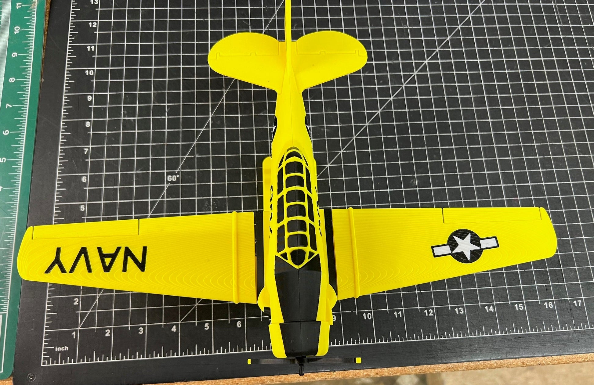 Yellow model airplane with 'NAVY' on a cutting mat