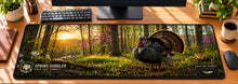 Turkey Woods Spring Gobbler Desk Mat in use on a warm wood office desk — overhead workspace view